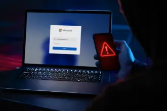 Portátil con pantalla de login de Microsoft y smartphone con icono de alerta roja, ilustrando el phishing de consentimiento en Microsoft 365.