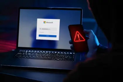 Portátil con pantalla de login de Microsoft y smartphone con icono de alerta roja, ilustrando el phishing de consentimiento en Microsoft 365.
